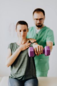 A therapist assists a patient with dumbbell exercises in a clinic setting.