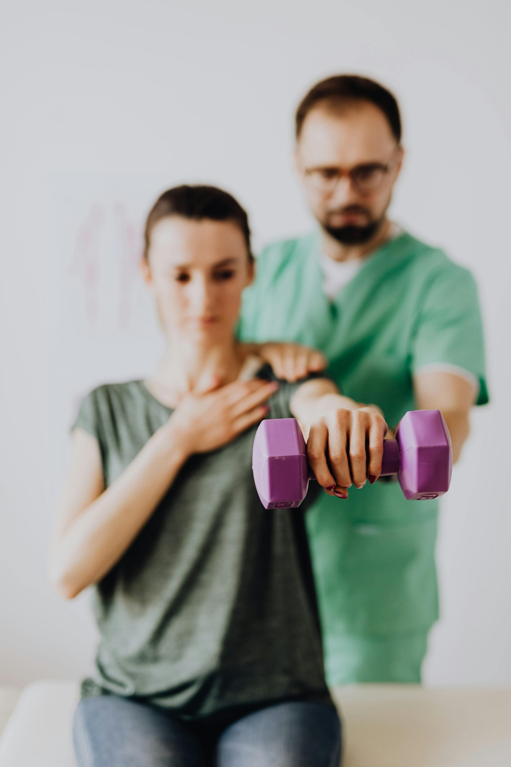A therapist assists a patient with dumbbell exercises in a clinic setting.